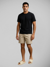 Modelo Carlos veste calça branca e camiseta clara, combinando com sandália slide em tom areia para um visual clean e elegante com inspiração urbana.