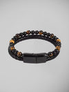 Pulseira masculina com couro trançado preto e contas olho de tigre centralizada sobre fundo branco