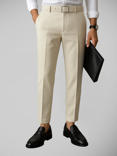 Homem vestindo camisa branca e calça social off white, segurando uma pasta de couro preta em uma sala sofisticada, destacando o estilo elegante e minimalista da Vestyge.