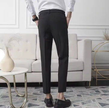 Close da calça de alfaiataria preta em homem com camisa branca e relógio escuro, destacando corte reto e acabamento refinado, em fundo branco.